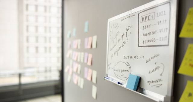 A whiteboard hangs on a wall next to sticky notes, populated with digital transformation strategy planning